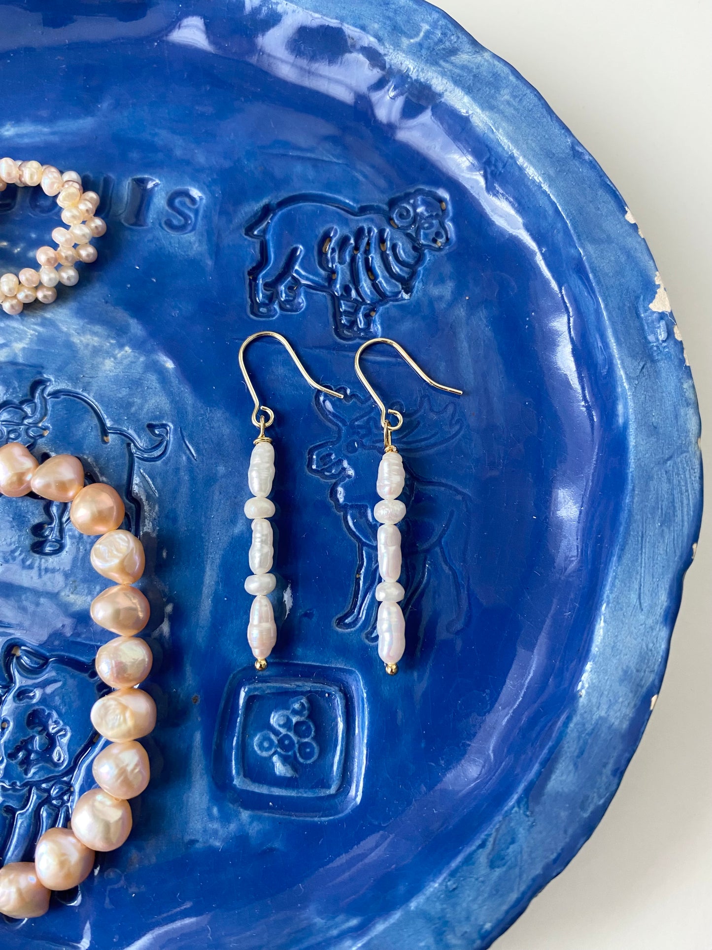 Merelle Pearl Longelle Süsswasserohrringe auf blauem Keramikteller – Lunara Edelsteinschmuck Schweiz