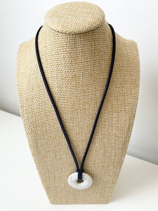 Nivora Howlith Halskette — Weiße Howlith‑Halskette mit rundem Donut‑Anhänger und dunklem Band, präsentiert auf einer beigen Schmuckbüste in minimalistischem Stil.