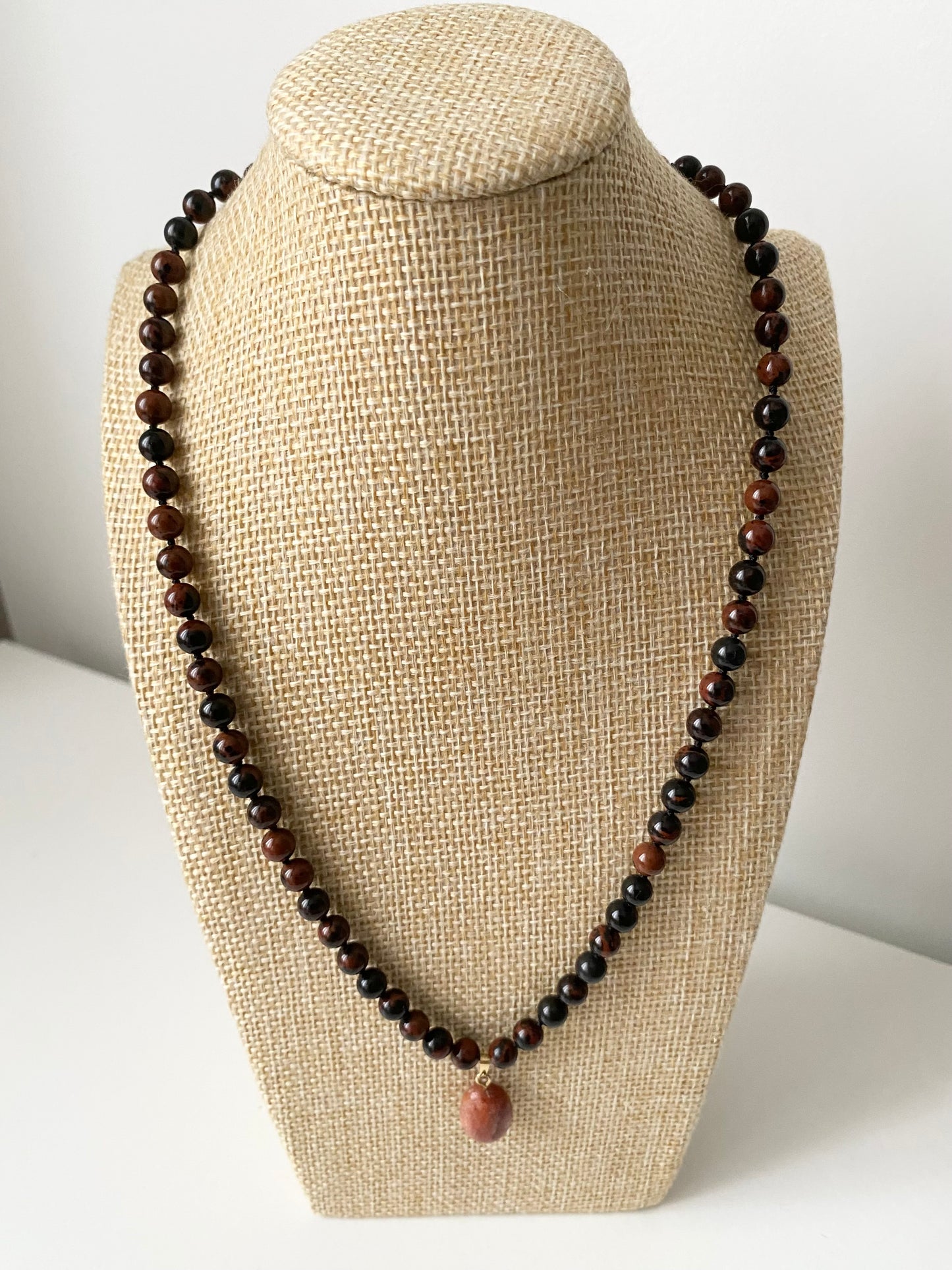 Valene Obsidian Halskette — Dunkle Obsidian‑Halskette mit runden Naturstein‑Perlen und warmem Sonnenstein‑Anhänger, präsentiert auf einer beigen Schmuckbüste in minimalistischem Stil.