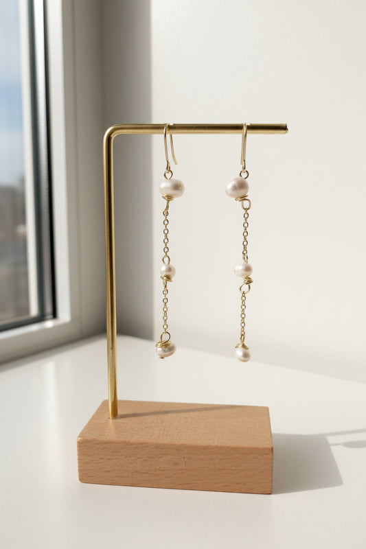 14K Gold Filled &amp; 18K Gold Plated Ohrringe mit zarten Ketten und drei organischen Süßwasserperlen, präsentiert im warmen Tageslicht auf einem minimalistischen Ständer.