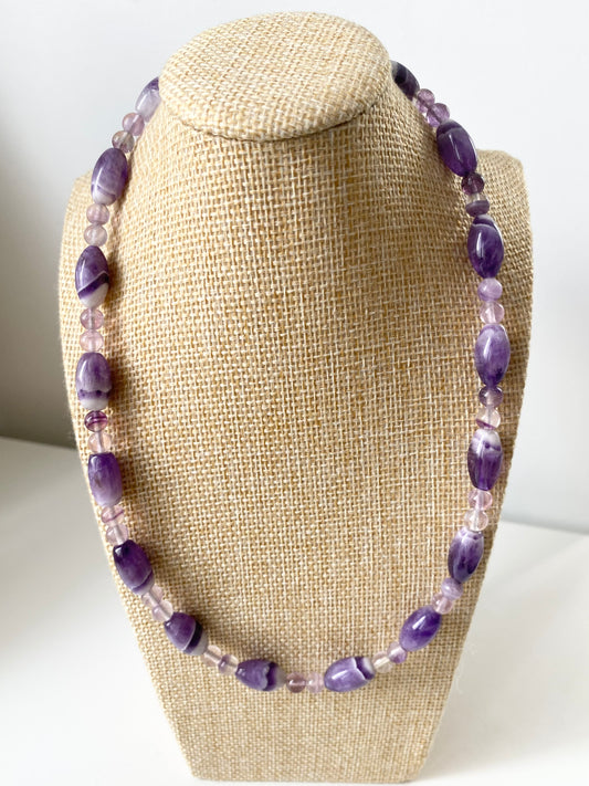 Aurelle Amethyst Halskette — Violette Amethyst‑Halskette mit ovalen und runden Naturstein‑Perlen in verschiedenen Purpurtönen, präsentiert auf einem beigen Schmuckbüsten‑Display.