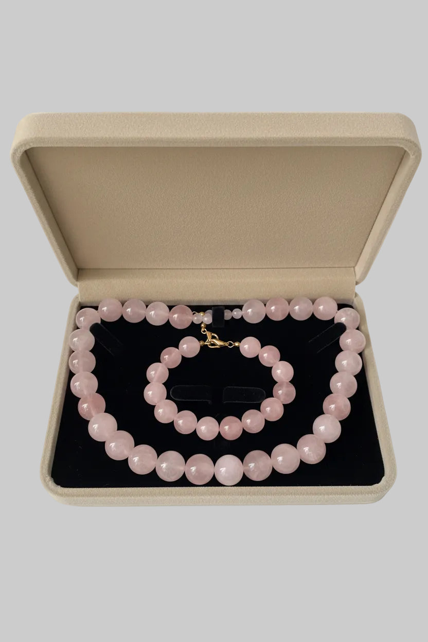 Aureline Rosé Rosenquarz Set — Halskette und Armband aus runden, hellrosa Rosenquarz-Natursteinperlen mit Goldverschluss, präsentiert in einer schwarzen Samtschatulle.