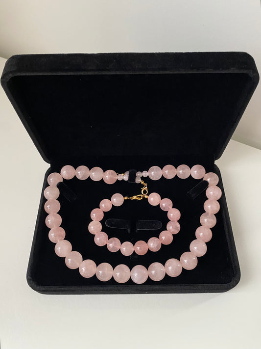 Aureline Rosé Rosenquarz Set — Halskette und Armband aus runden, hellrosa Rosenquarz-Natursteinperlen mit Goldverschluss, präsentiert in einer schwarzen Samtschatulle.