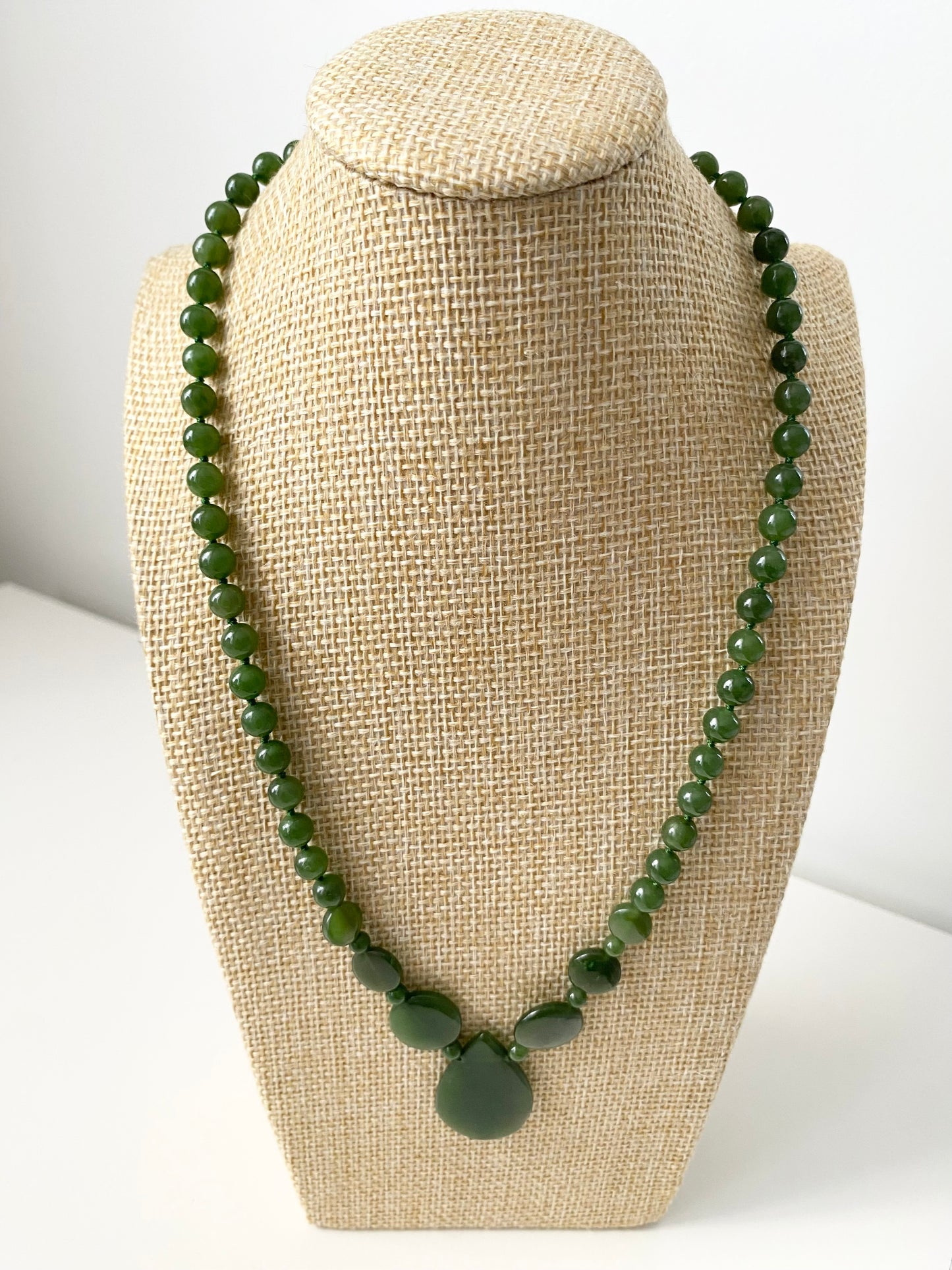 Lara Jade Halskette — Grüne Jade‑Halskette mit runden, ovalen und tropfenförmigen Naturstein‑Elementen sowie zentralem Anhänger, präsentiert auf einer beigen Schmuckbüste in minimalistischem Stil.