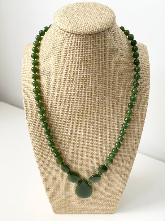 Lara Jade Halskette — Grüne Jade‑Halskette mit runden, ovalen und tropfenförmigen Naturstein‑Elementen sowie zentralem Anhänger, präsentiert auf einer beigen Schmuckbüste in minimalistischem Stil.
