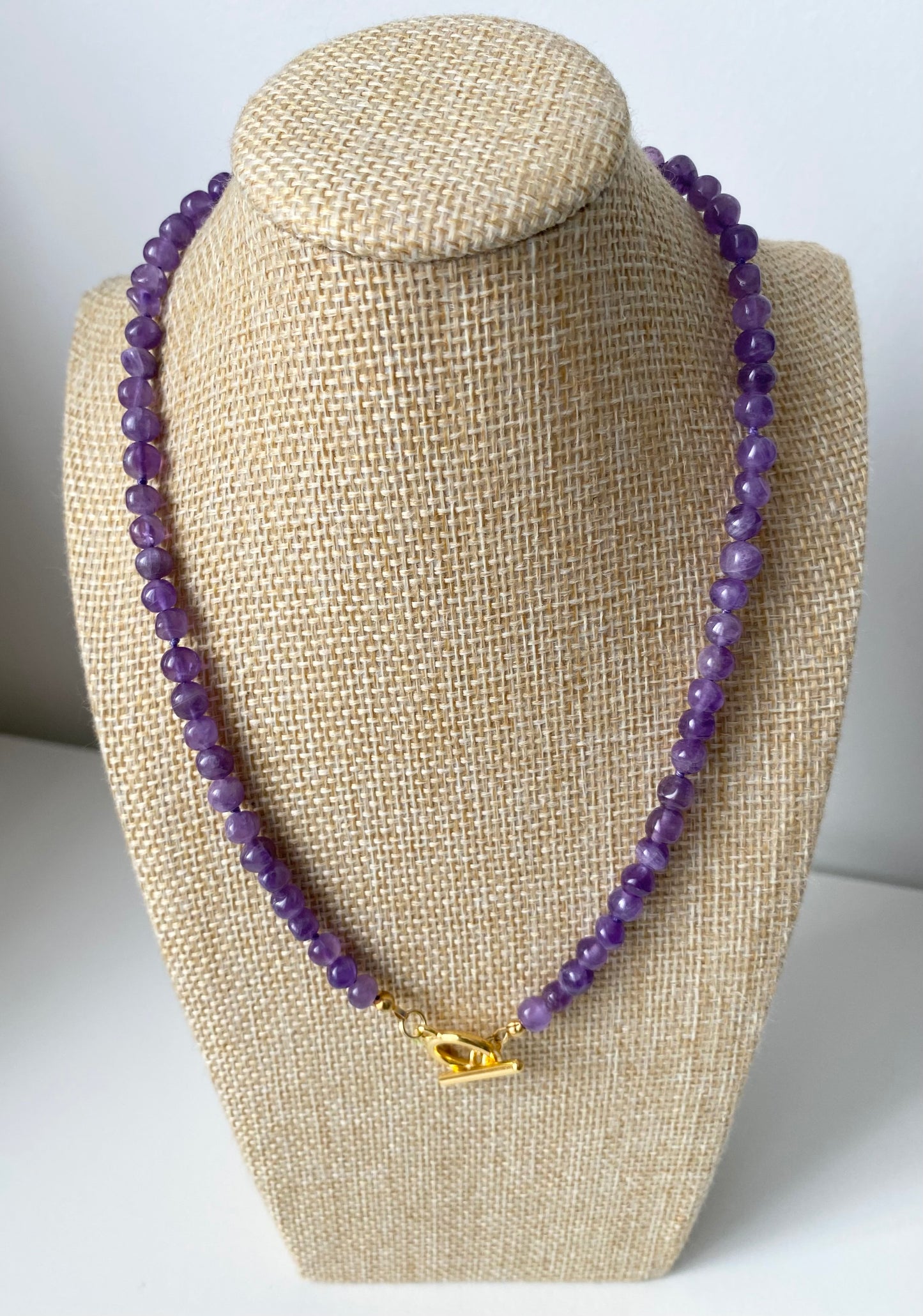 Amethyst Halskette Arisa mit polierten violetten Naturstein‑Perlen und goldfarbenem Toggle‑Verschluss, 44 cm, präsentiert auf Schmuckbüste.