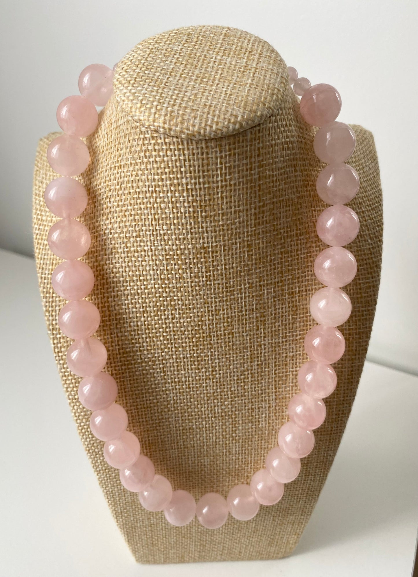 Aureline Rosé Rosenquarz Set — Zartes Rosenquarz‑Set aus Halskette und Armband mit runden, hellrosa Naturstein‑Perlen, präsentiert auf einer beigen Schmuckbüste in minimalistischem Stil.