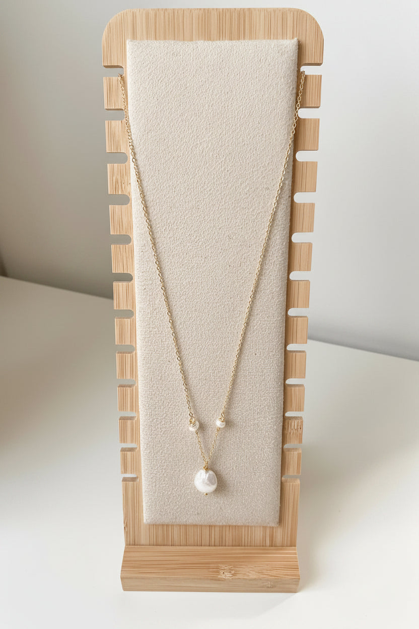 Merelle Pearl Rondelle Süsswasserohrringe mit kleiner Rondelle‑Perle und grosser barocker Süsswasserperle in goldfarbener Fassung, präsentiert auf einem minimalistischen Stoff‑Schmuckständer.