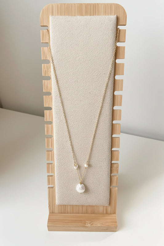 Merelle Pearl Rondelle Süsswasserohrringe mit kleiner Rondelle‑Perle und grosser barocker Süsswasserperle in goldfarbener Fassung, präsentiert auf einem minimalistischen Stoff‑Schmuckständer.