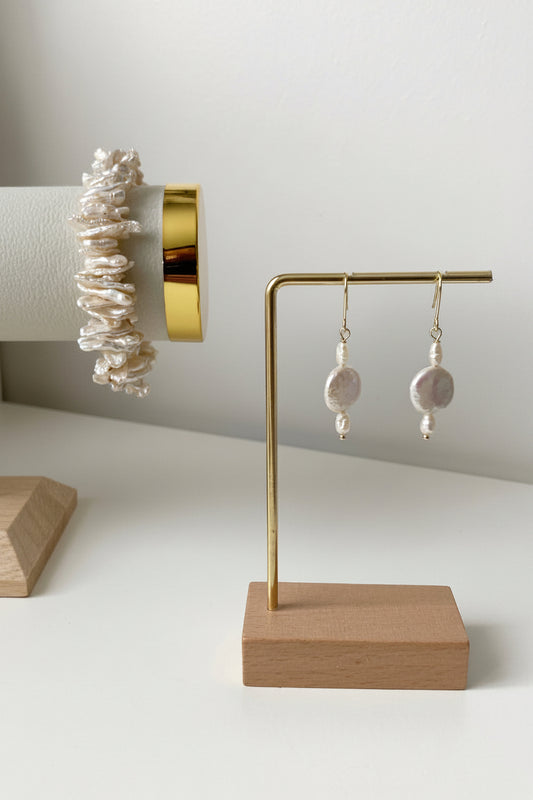 Merelle Pearl Rondelle Süsswasserohrringe mit kleiner Rondelle‑Perle und grosser barocker Süsswasserperle in 14K‑Gold‑Filled Fassung, präsentiert auf minimalistischem Schmuckständer.